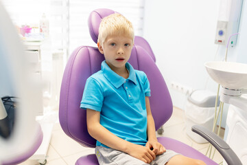 a child a five year old boy in a blue t shirt is sitting in a lilac chair in a white office