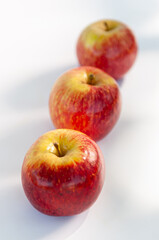 Three red apples with focus on the foreground and blur background on a white table. Selective focus