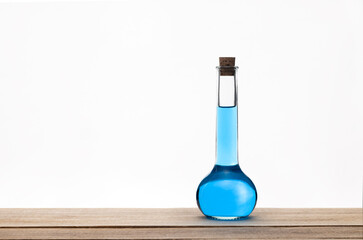 Glass vintage bottle with a brown cork and blue liquid on a wooden table with white background. Alchemy concept. Space for text.