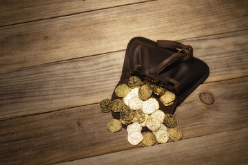 Old medieval pouch with poured coins on the old wooden table. Leather purse on rustic wooden background.