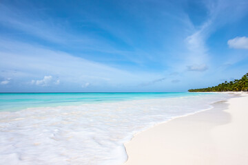 The edge of the wave on the white sand of a wild tropical beach. Blue sky and turquoise water of...