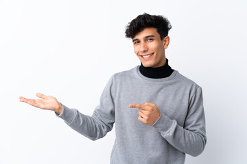 Young Argentinian man over isolated white background holding copyspace imaginary on the palm to...