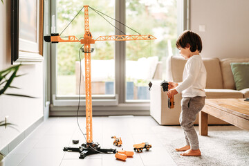 Little toddler boy playing with big construction building crane toy at home in living room. Child...