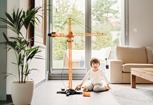 Little happy toddler boy playing with big construction building crane toy at home in living room. Child leisure activity, creative game, using imagination.