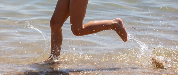 Fototapeta premium Splashes from the feet of a girl running through the water