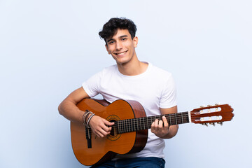 Obraz premium Young Argentinian man with guitar over isolated blue background showing ok sign with fingers