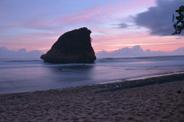 Sea long exsposure at sunset with cloudy sky and rock cliff in the middle. in the South Java Beach