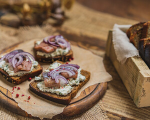 Sandwich with whole grain bread salted herring, cottage cheese and red onion on old rustic cutting board. Selective focus, copy space.