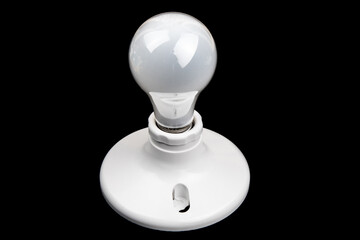 an incandescent light bulb in a simple white light fixture on a black background