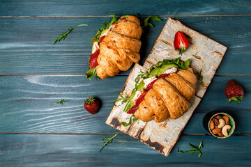 Breakfast, business lunch, sandwiches Croissant with strawberries and soft cheese with mold brie camembert on wooden background. banner menu recipe top view