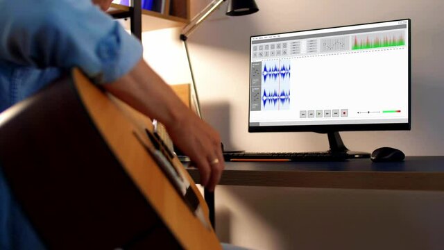 leisure, music and technology concept - young man or musician playing guitar and recording sound with computer program at home studio