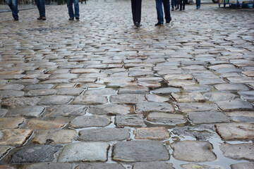 A close-up on a wet durable stone pebbled walkway, cobblestone pedestrian shared street of an old city.