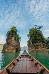 View from the wooden Thai style boat in a dam with emerald water and white big stonds. There is a channel through the limestone, clear blue sky. Ideas for traveling background with copy space.