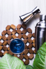 Top view. Blue cocktail in glass with ice and cocktail shaker and green leaves on wooden table. Summer refreshing cocktails drinks. Copy space and space for text