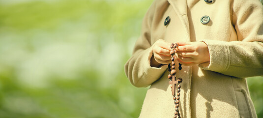 Young girl praying and holding a wooden rosary. Copy space for text or design.