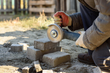 A man saws off paving stones with an angle grinder. Street work - obrazy, fototapety, plakaty