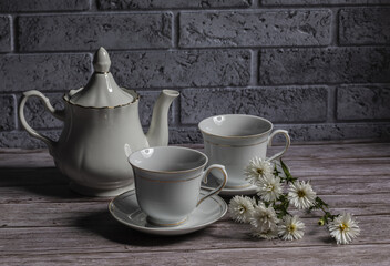 Teapot and tea cups on a wooden table and a sprig of white Aster.