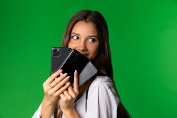 Teen schoolgirl with various smartphones. Content female teenager holding assorted modern mobile phones and looking away against green background 