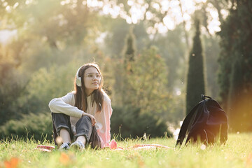 Cute teenage girl is sitting in the park on a sunny day and listening to music   