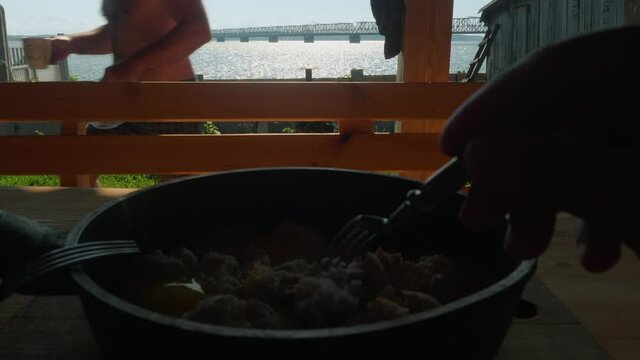 View of river and huge bridge over it. Pan with meat pieces is at foreground, man's hand takes one peice of meat.