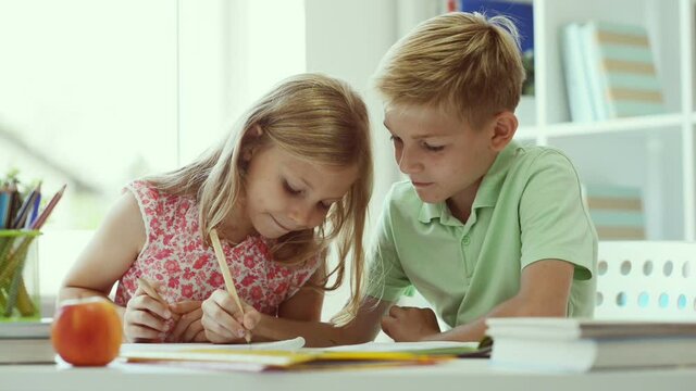 Two cute schoolchildren boy and girl doing homework at home