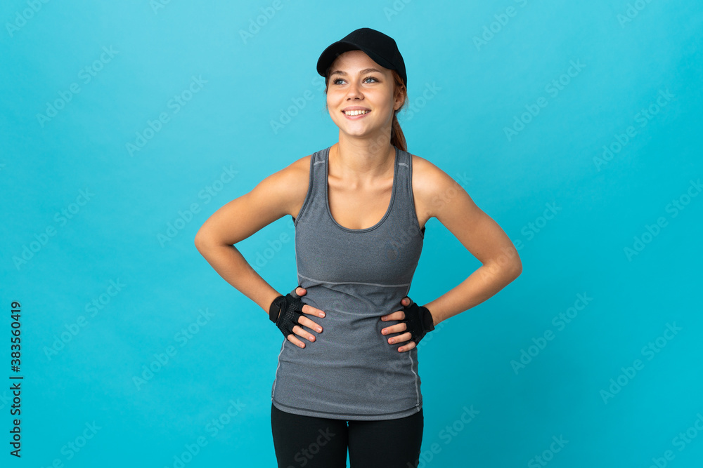 Wall mural teenager sport russian girl isolated on blue background posing with arms at hip and smiling