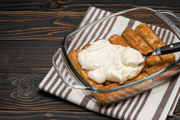 tiramisu dessert cooking - Traditional Italian Savoiardi ladyfingers Biscuits and cream in glass baking dish on wooden background