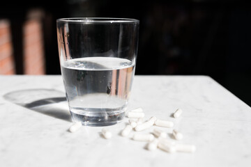 White pills tablets on a white marble table isolated glass of water bright light health