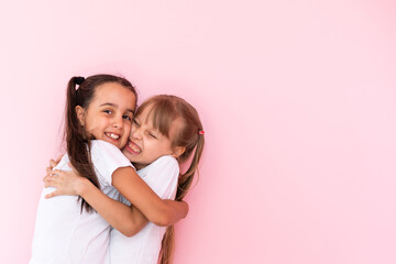 Two little girls hugging each other. Isolated on on a pink background