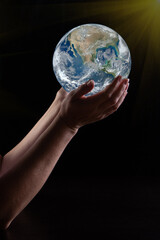 women's hands hold the planet Earth with interesting lighting. Low key. Elements of this image furnished by NASA. vertical frame