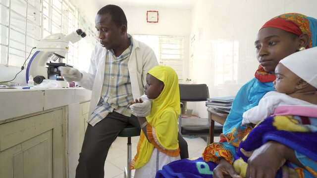 Doctor taking blood sample from female child in clinic. Africa