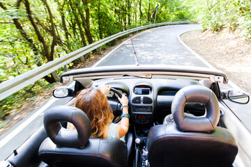 Young woman driving convertible car on summer day through nature. Enjoying beautiful day.Female...
