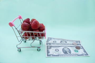 Shop trolley full of ripe red strawberry. Under the wheels of the trolley on a blue background are...