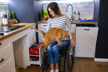 Disabled young woman in kitchen with cat on her lap
