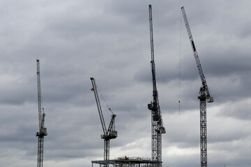 Four tower cranes are seen side by side on a construction site in London, United Kingdom, during a cloudy day.