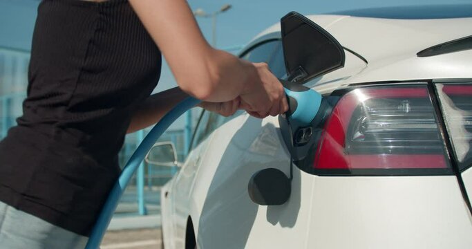 Female hand plugs in a charging cable in an electric car.