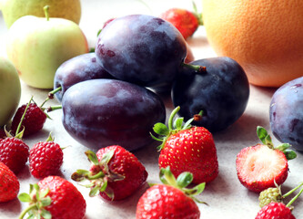 Fresh plums with strawberries on the background of apples and citrus, close - up, side view-the concept of cooking delicious dishes from fresh berries and fruits