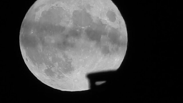 Full lunar wobble harvest moon crater surface closeup passing rooftop silhouette skyline