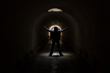 A man in a dark underground tunnel is looking for a way out and raises his hands to the sky asking for help.