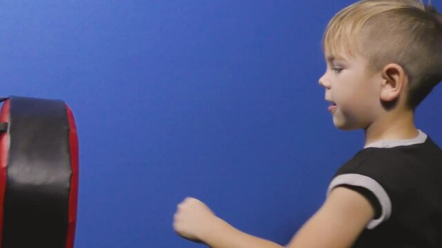 Boy athlete trains punches on the simulator on a blue background