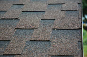 A close-up a roof covered with copper brown bitumen, asphalt laminated, dimensional, or architectural roofing shingles.  Asphalt shingles background.