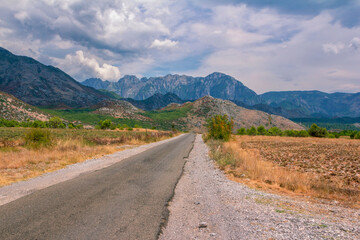 Fototapeta na wymiar Summer landscape – valley and road in Albanian mountains, agricultural fields and gray clouds on the sky.
