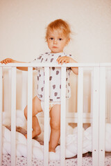 a picture of a cute happy one-year-old boy with brown eyes standing in bed just waking up in the morning