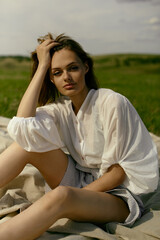 Nice picnic on the grass. Young beautiful woman in the middle of green field. Summer landscape, good weather. Windy day with sun and clouds. Cotton white suit eco style. 