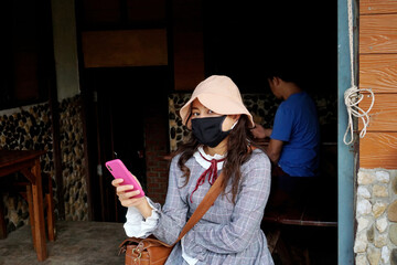 Obraz premium woman wear face mask holding mobile phone sit away from others, social distancing, covid-19 prevention