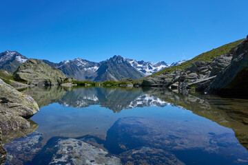 Bergsee blau und klares Wasser spiegelnd andere Berge
Spiegelung Alpen mit Schnee