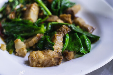 Stir-fried kale with crispy pork on white palte.