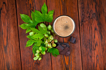 Glass of dark stout beer with natural green hop leaves and chopped chocolate on a wooden table. Top view.