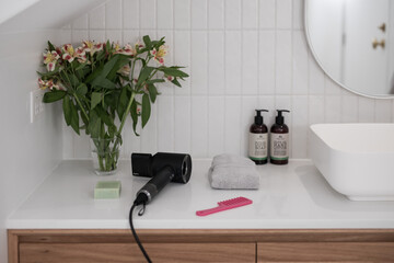 Modern black stylish hair dryer on a white stone vanity top with simple flowers in a vase - obrazy, fototapety, plakaty