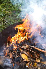 Burning in  barrel of autumn yellow maple leaves with flames and charcoals, the view from above, a lot of smoke, goodbay autumn summer, autumn mood
